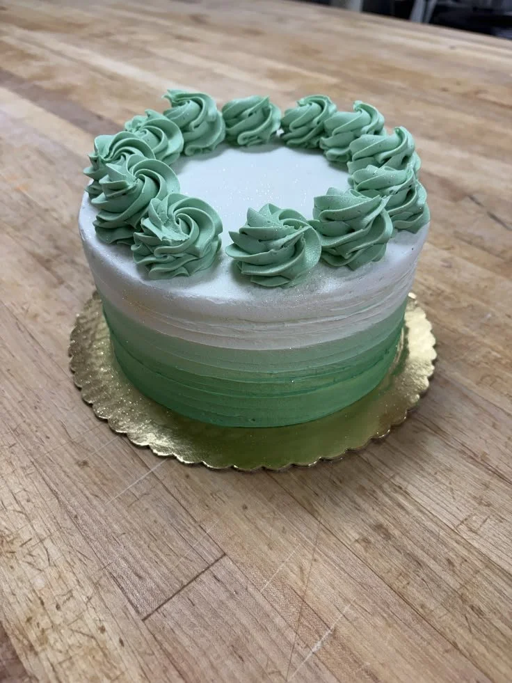 Decorative cake with green and white gradient frosting topped with green piped swirls, placed on a wooden surface.