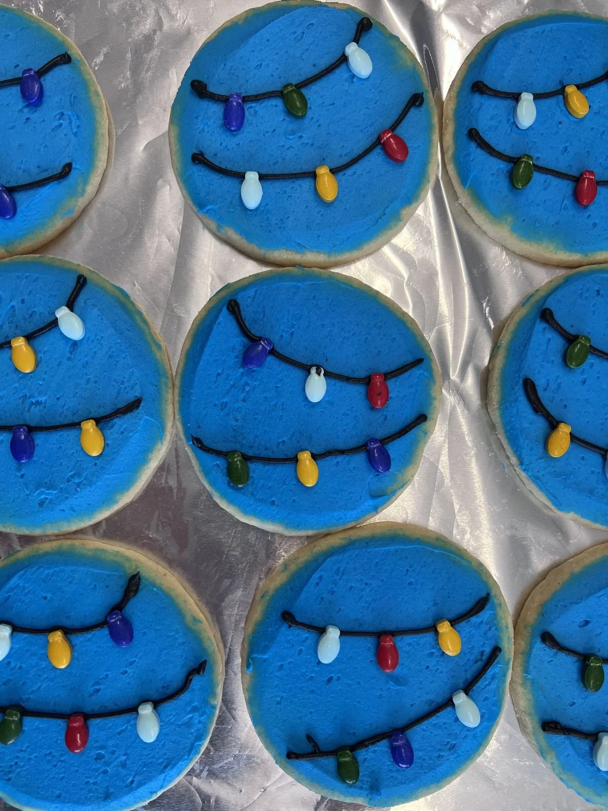 Collection of cookies decorated with blue icing and black icing to resemble string lights with colorful edible light bulbs.