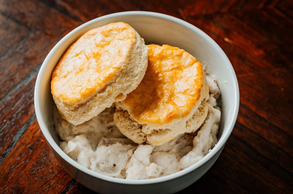Biscuits served with sausage gravy in a white bowl, on a wooden table.