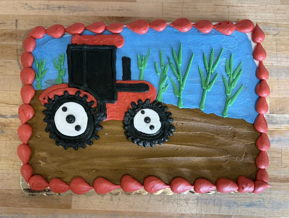 Decorative cake with a tractor and fields, featuring red, black, green, blue, and brown frosting.
