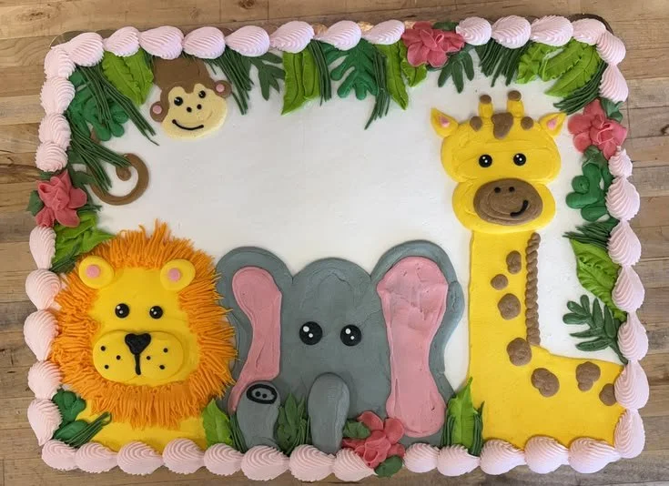 Decorative cake with colorful animal designs including a lion, elephant, giraffe, and a monkey head in the corner, with a green border.
