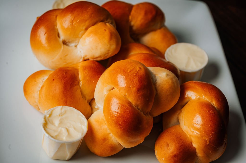 A plate of buttery, golden-brown dinner rolls with small cups of butter on the side.