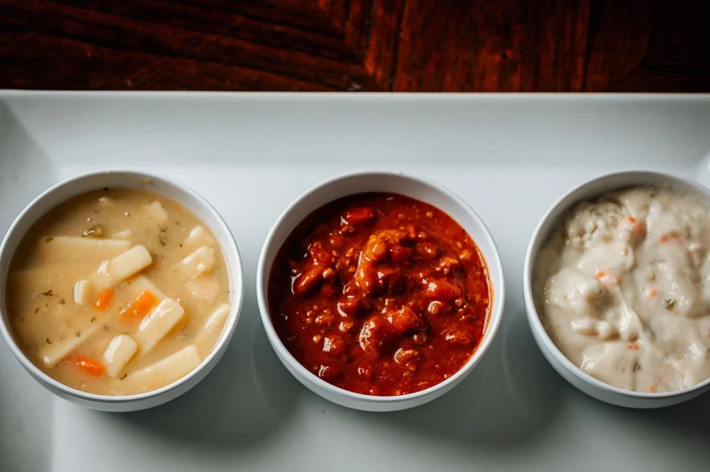 Three bowls of soup on a white tray.