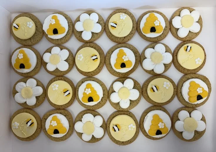 A tray of decorated cookies featuring bee and flower themes with white, yellow, and black icing details.