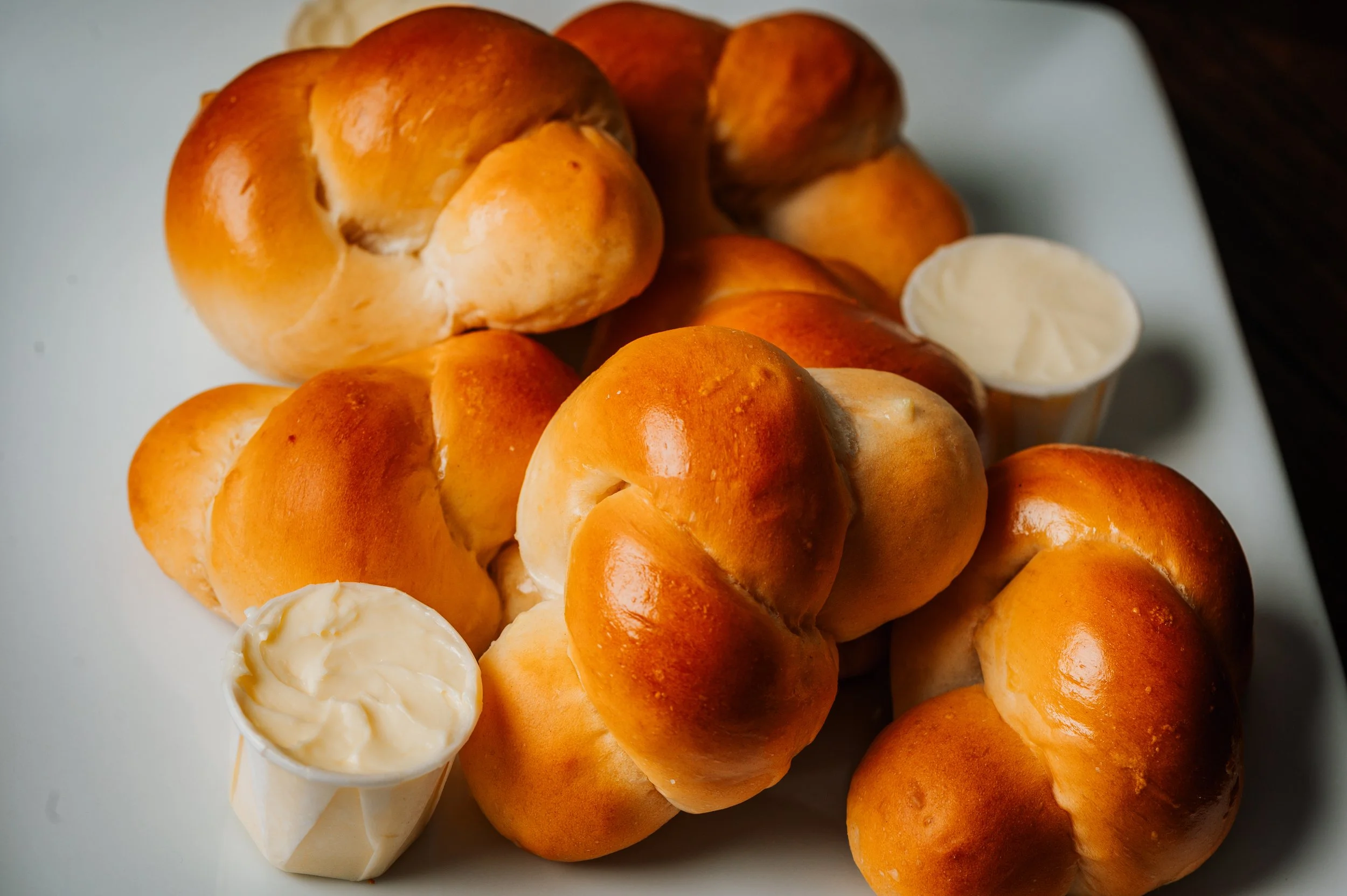 A plate of soft challah dinner rolls with a bowl of butter.