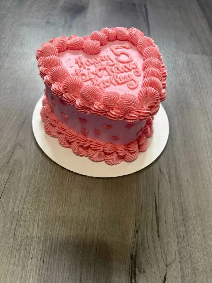 Heart-shaped pink cake with raspberry-colored frosting and a message that reads 'Happy 5th Birthday, Hayley' on top.