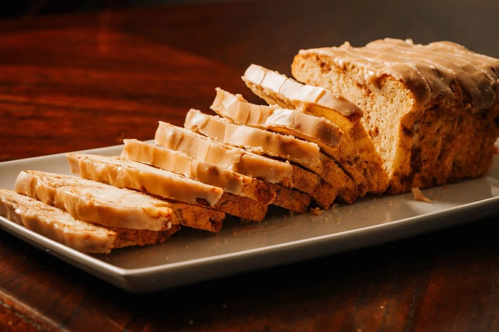 A loaf of glazed bread with slices cut and arranged on a white rectangular platter.