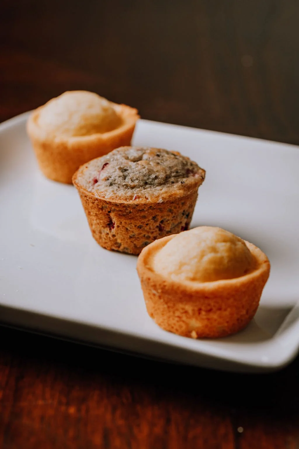 Three assorted muffins on a white rectangular plate.
