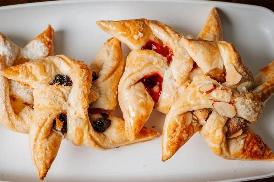 A variety of windmill pastries with fruit fillings, some topped with sliced almonds, on a white rectangular plate.