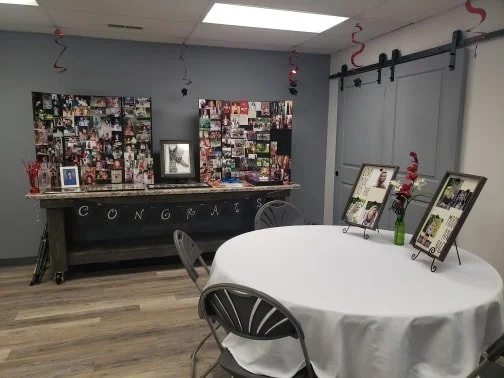 Room decorated for celebration with a table, photo display, and a congratulatory sign.