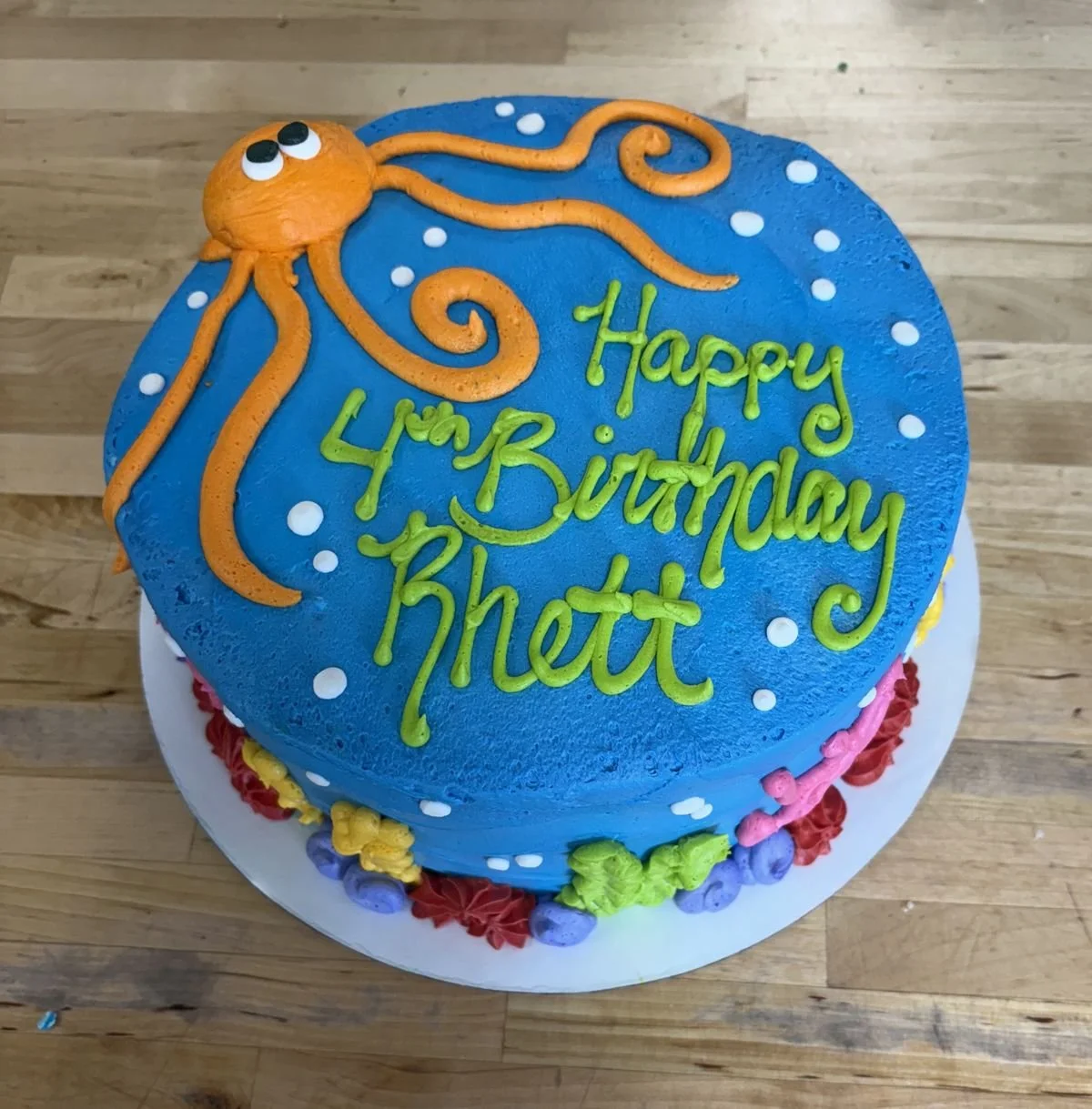 Colorful birthday cake with a blue top decorated with an orange octopus and green writing that says 'Happy 4th Birthday Rhett'.
