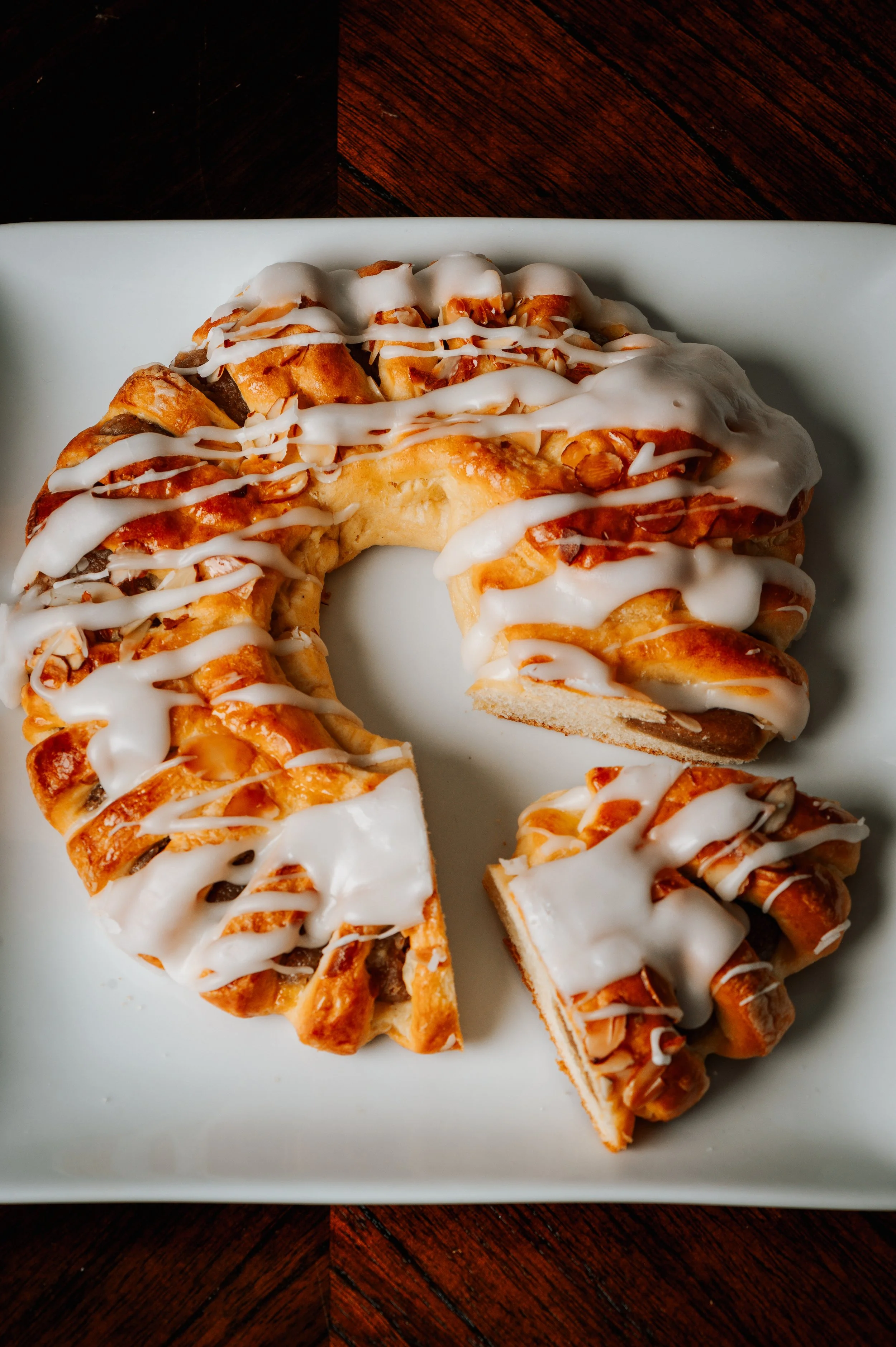 A white rectangular plate with sliced cinnamon roll cake drizzled with white icing, on a dark wooden table.