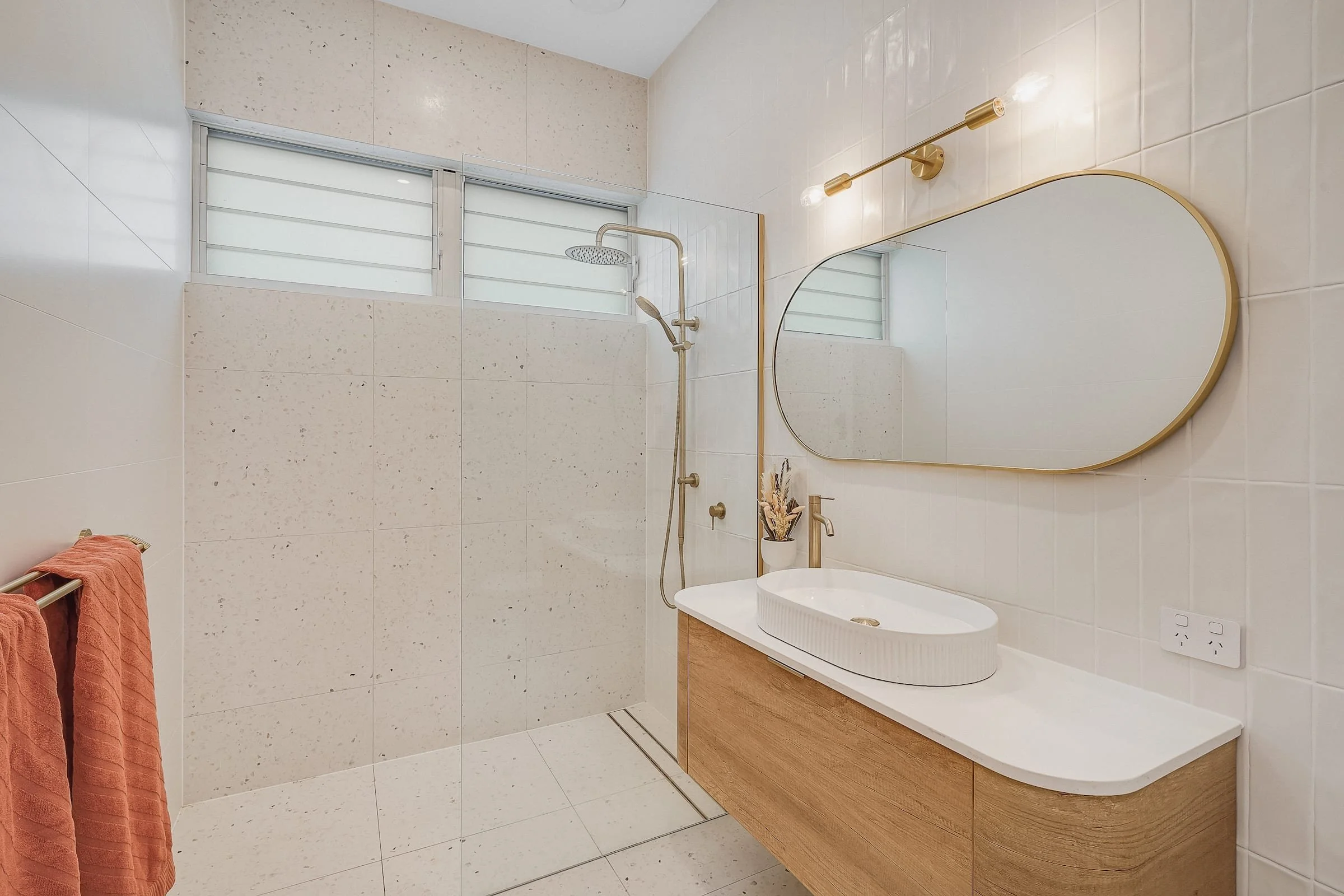 Modern bathroom renovation with curved mirror and vanity detail kitchen with a central island, three wooden stools, pendant lights, and a sliding door leading outside.