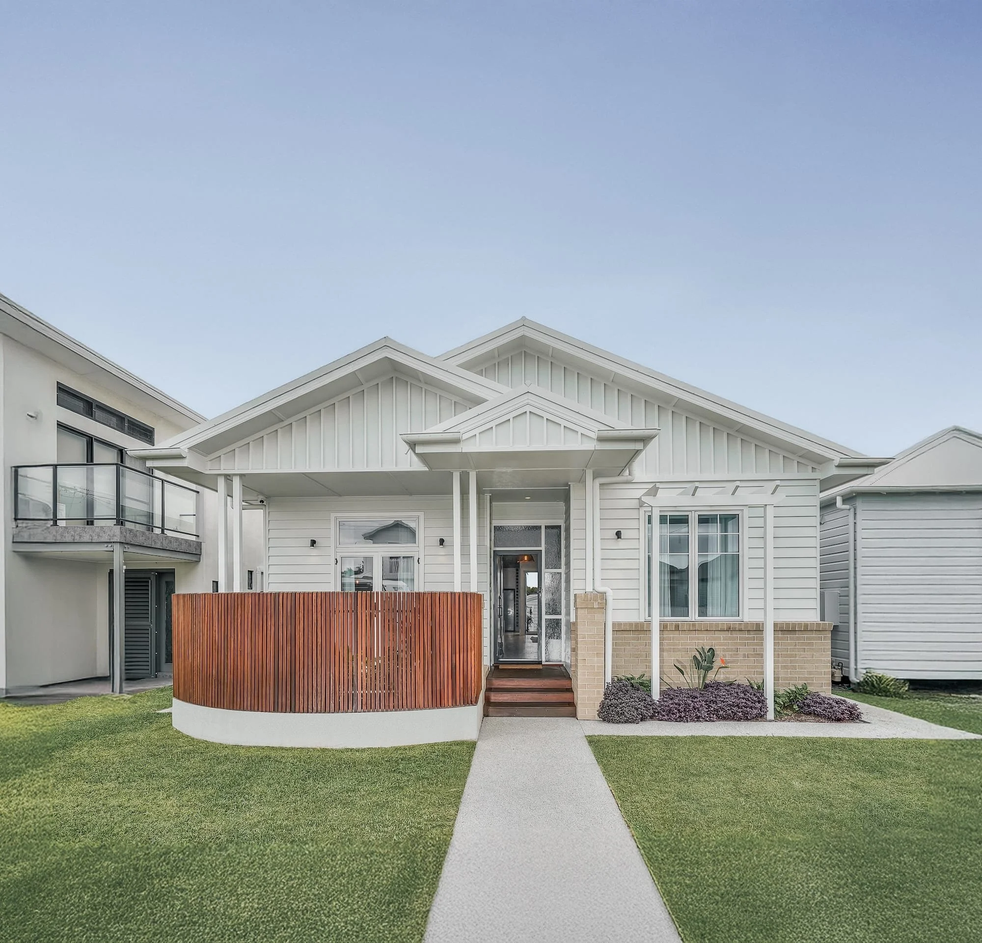 Front view of a modern, multi-story house with white exterior and multiple rooflines, featuring a small front porch and well-maintained lawn.