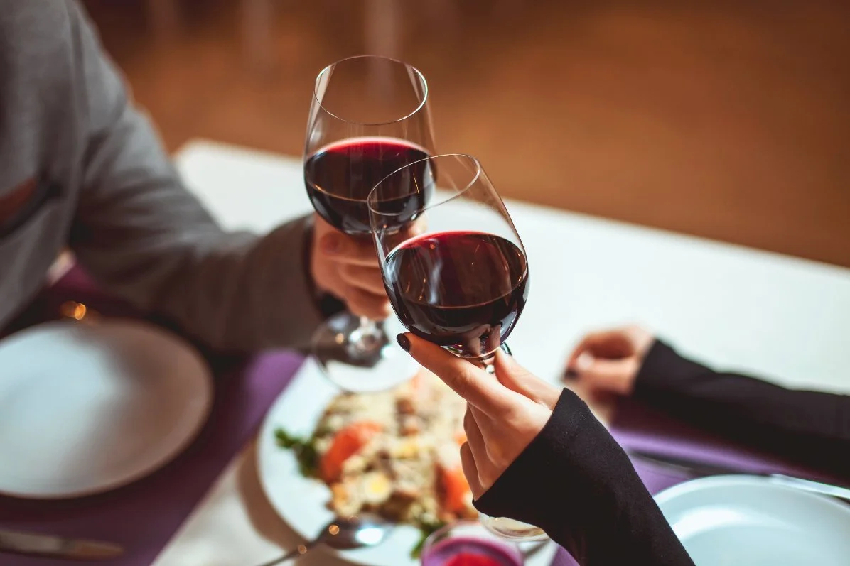 Beautiful young escort and client with glasses of red wine in luxury restaurant