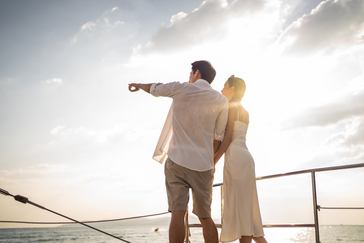 Attractive man and woman hanging out celebrating anniversary honeymoon trip while catamaran boat sailing during summer sunset.