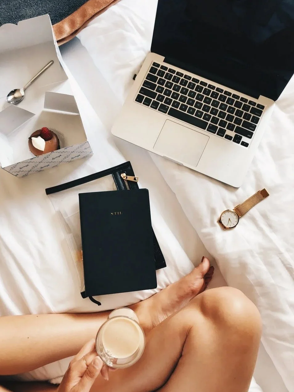 Woman on bed reading book and open laptop