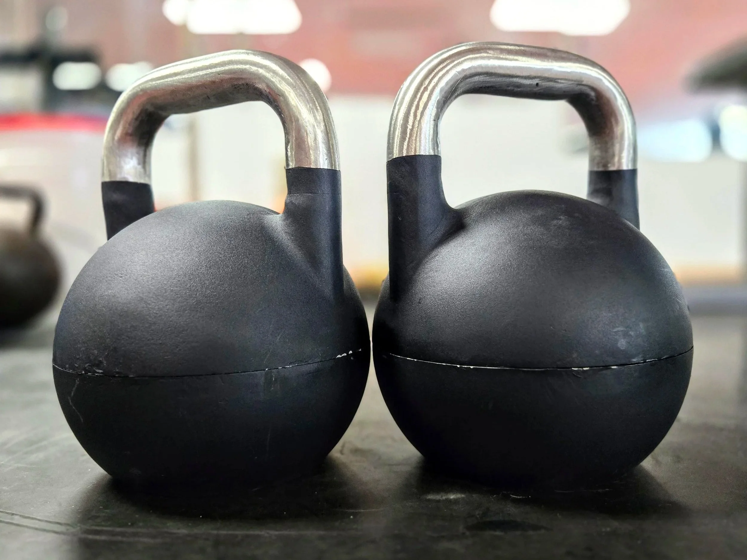 Two black kettlebells with silver handles placed on a dark surface.