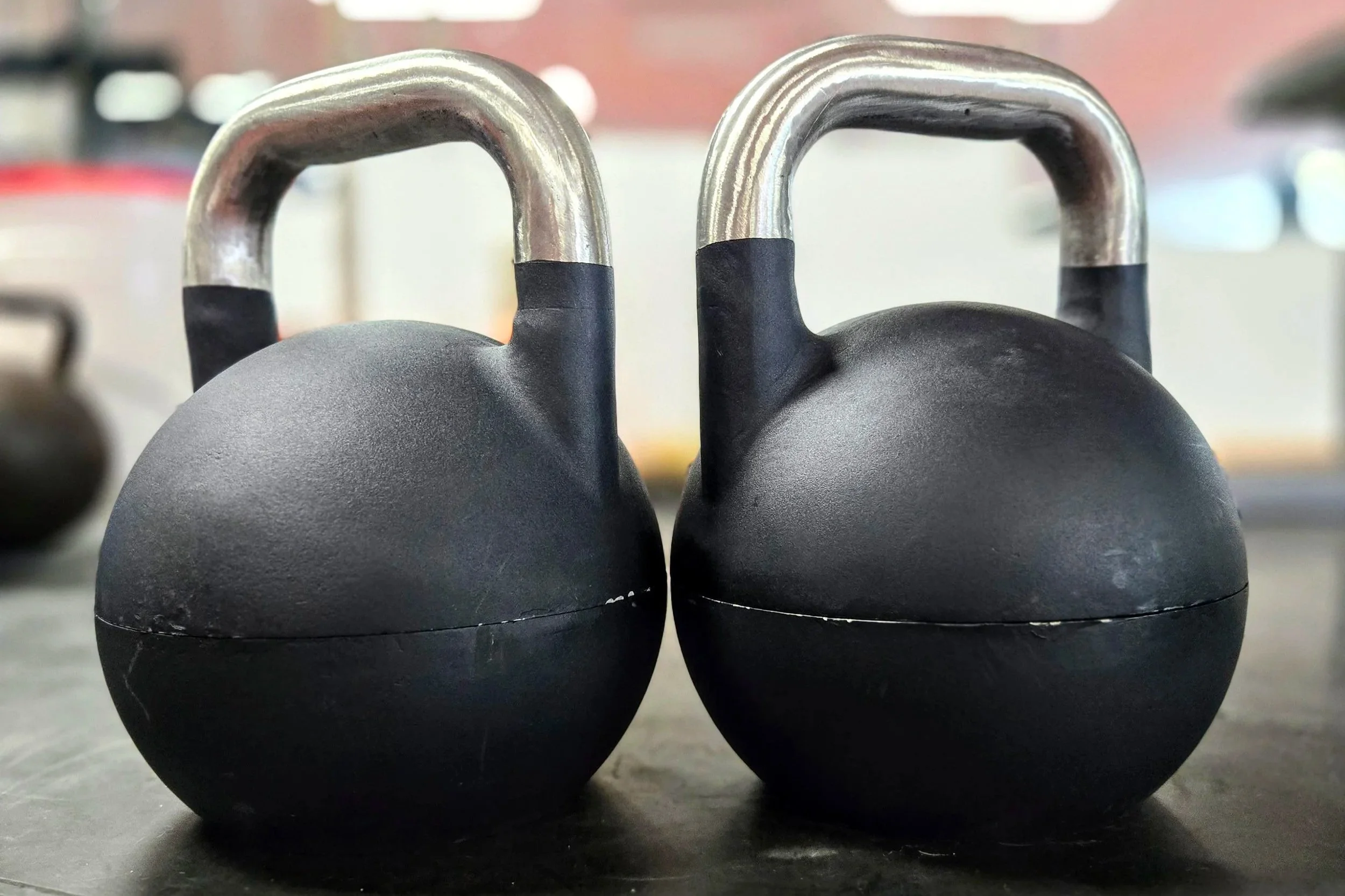 Two black kettlebells with silver handles placed on a black surface.