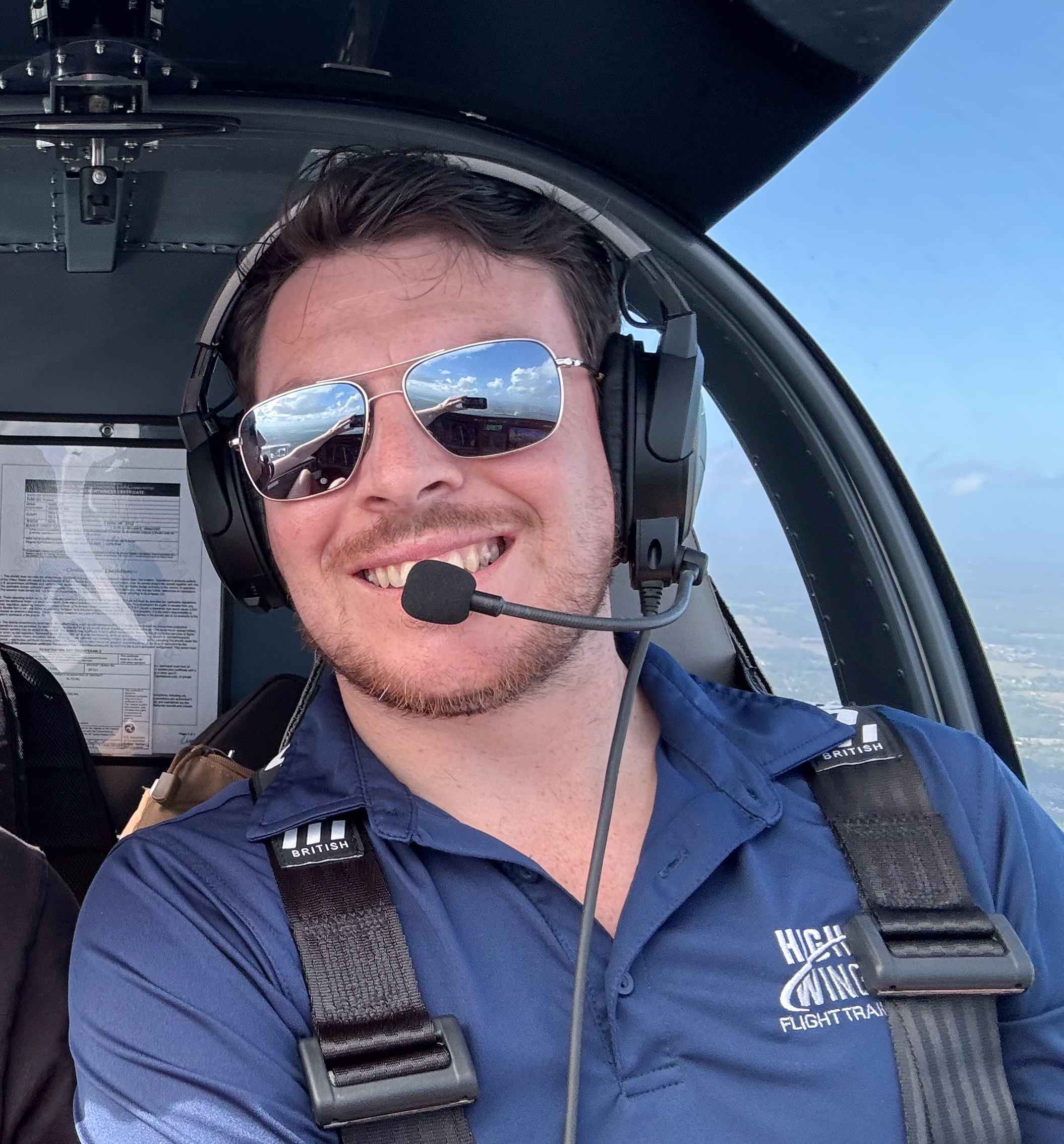 Pilot CFI wearing sunglasses and a headset, smiling inside the cockpit of an aircraft with a view of blue sky and clouds outside.
