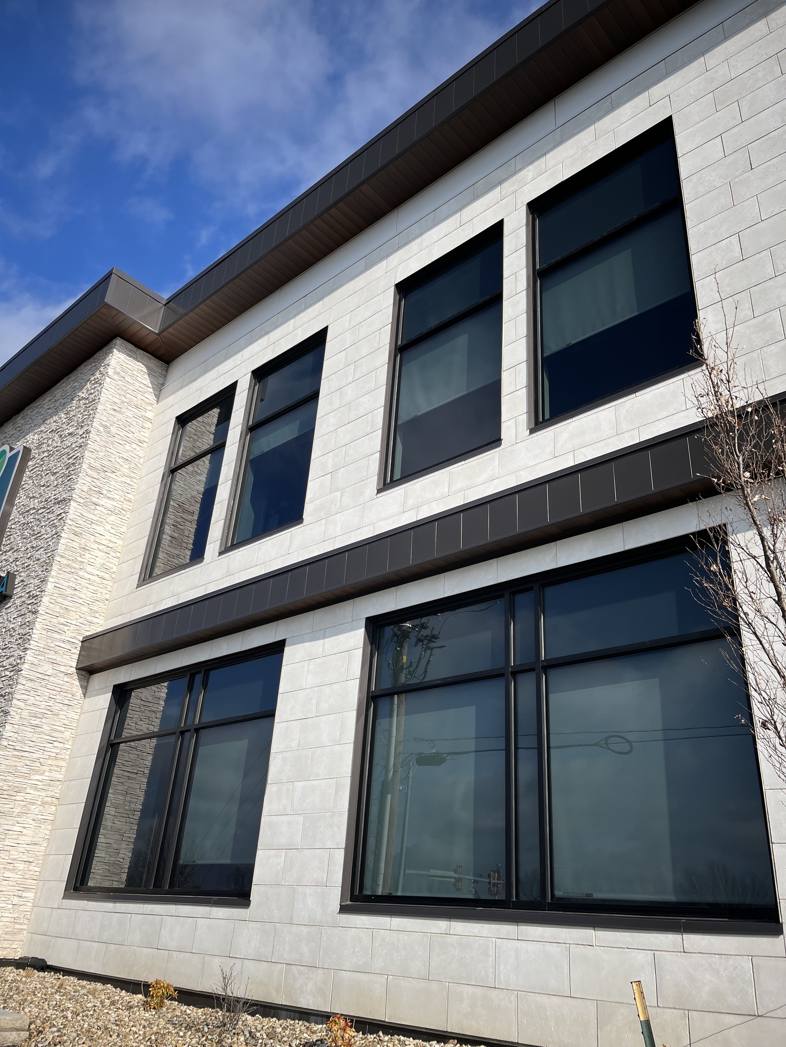 Modern building with large black-framed windows, light-colored masonry, and a dark roof under a blue sky.