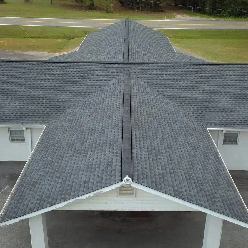 A close-up aerial view of a house's gray shingled roof, showing the intersection of different roof sections and part of the front porch.