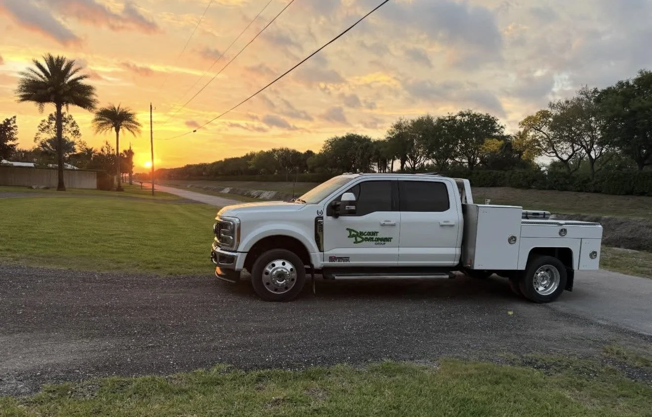 Discount Development Group branded contractor truck parked on a gravel road at sunset in South Florida, palm trees in the background.
