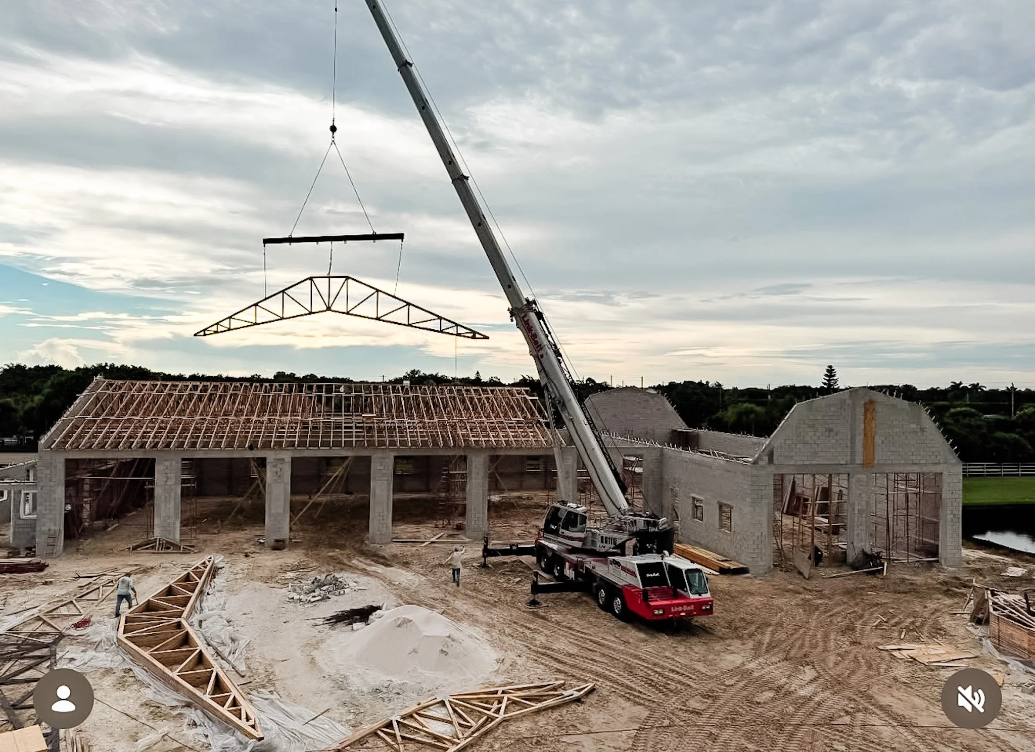 Discount Development Group crane lifting a steel truss during shell construction of an equestrian facility in Wellington, Florida, with workers and building materials on site.