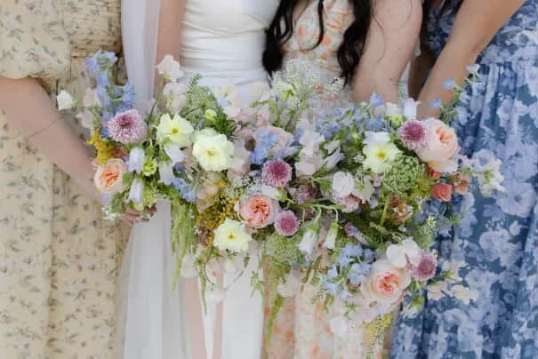 Close-up of women holding a large bouquet of mixed flowers at a wedding celebration.