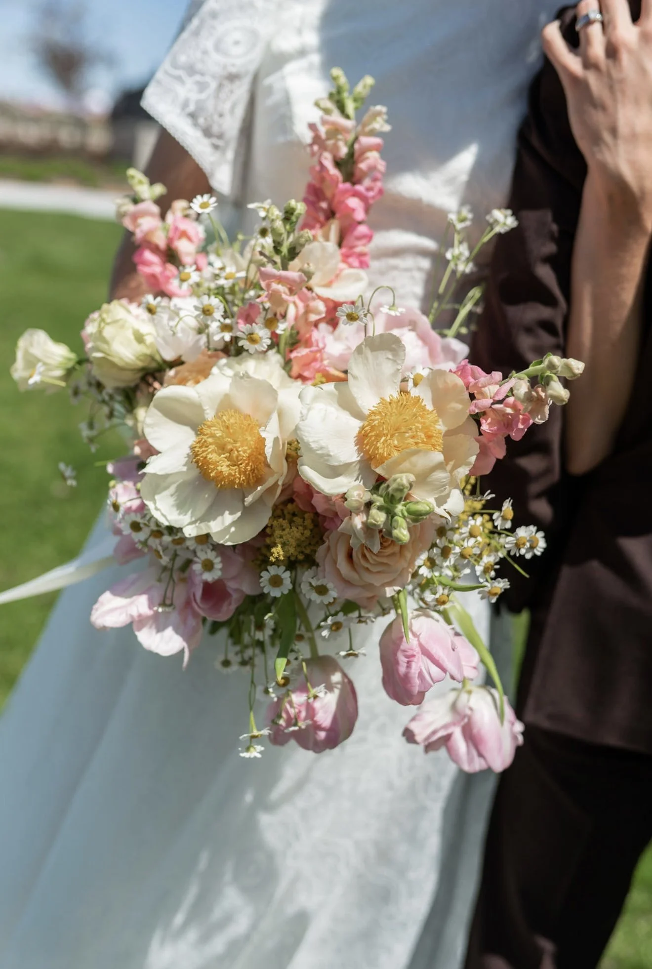 Person holding a bouquet of various pink, white, and yellow flowers outdoors.