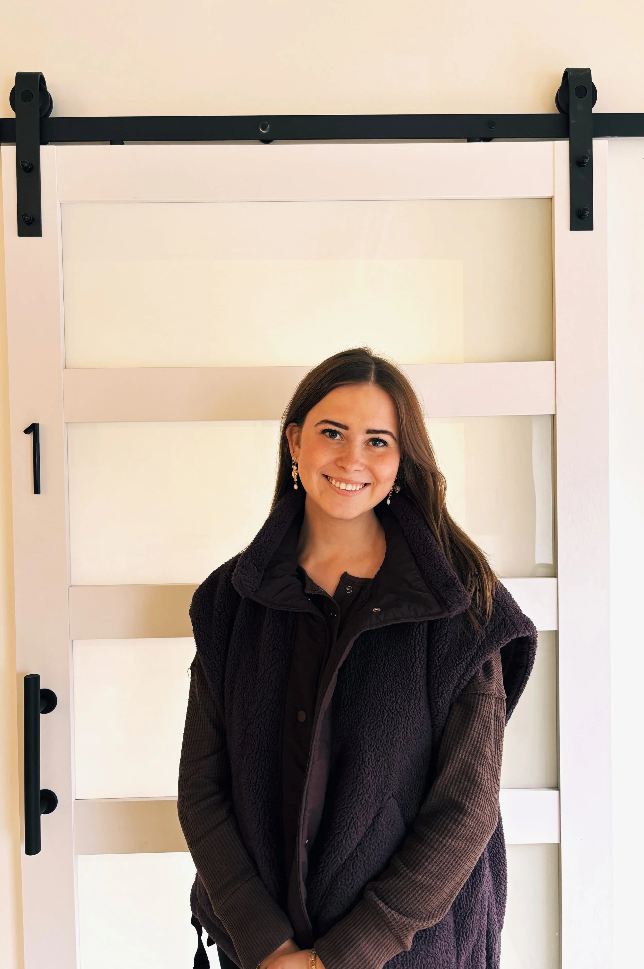 A woman with brown hair and earrings smiling in front of a sliding door with horizontal panels.