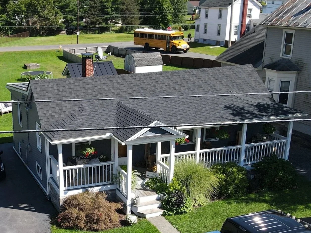 A house with a front porch, garden, and a yellow school bus parked nearby.