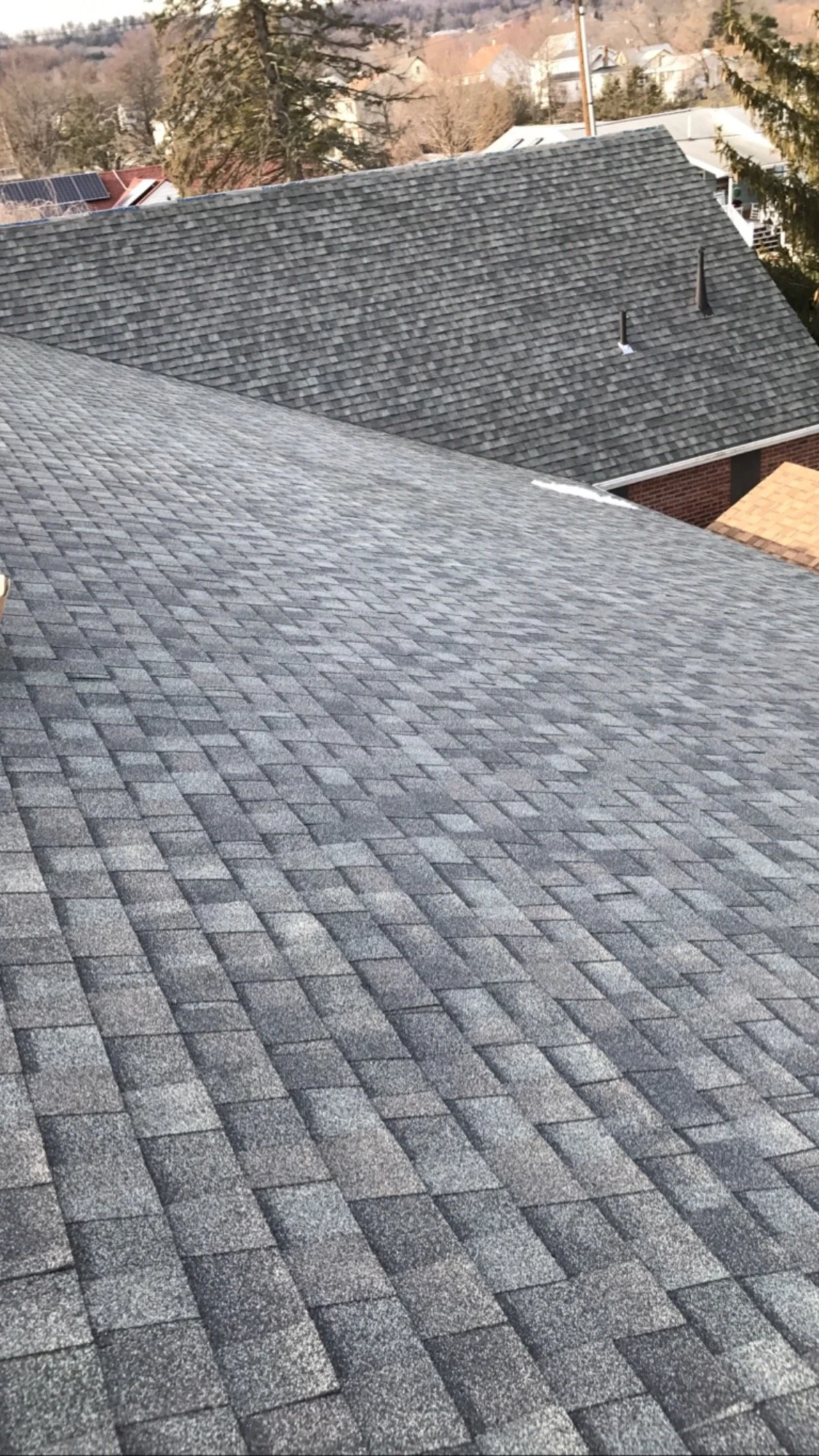 Multiple rooftops with asphalt shingles in different shades of gray, viewed from above during daytime.
