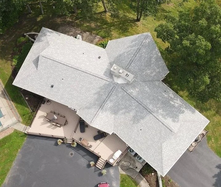 Aerial view of a house with a complex roof design, a deck with outdoor furniture, and a paved driveway with a pink car parked.