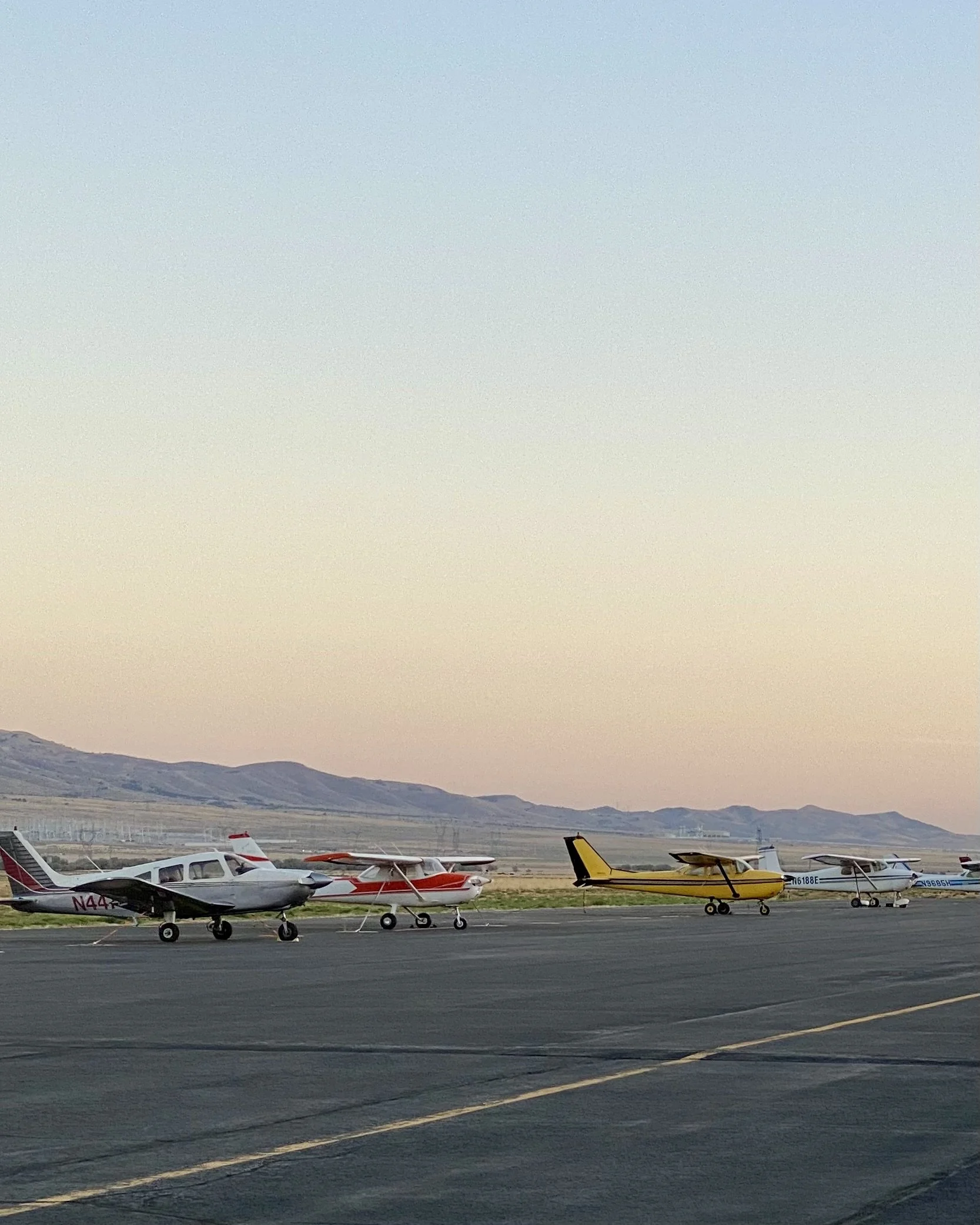 Small aircraft parked on an airstrip during sunset with mountains in the background.