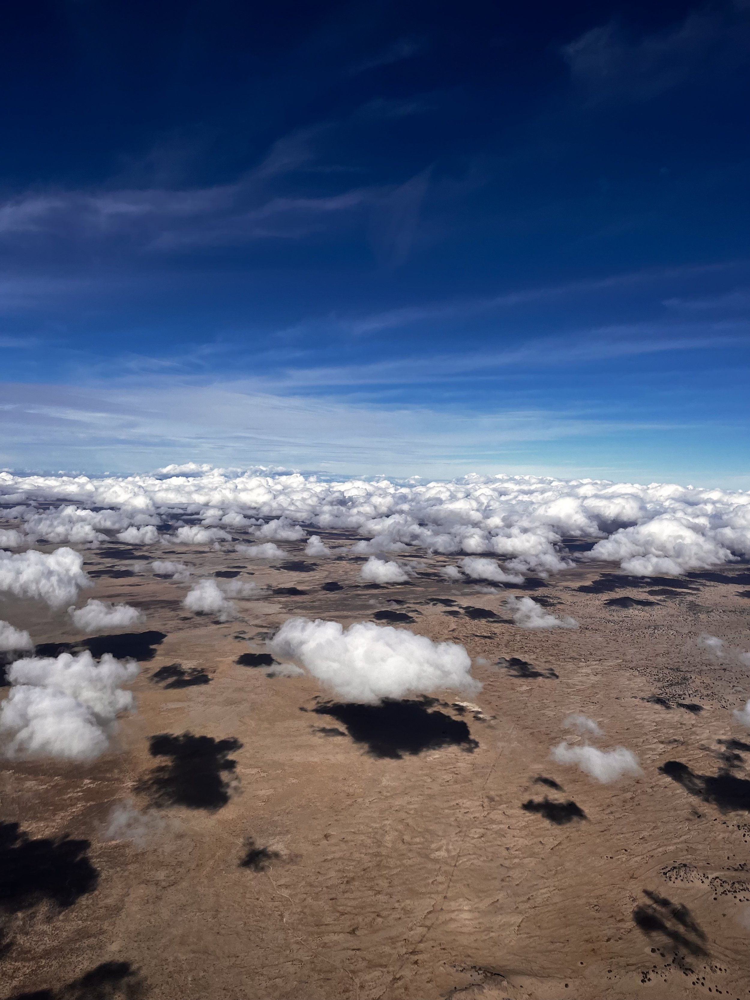 Aerial view of desert landscape with scattered clouds and a blue sky.