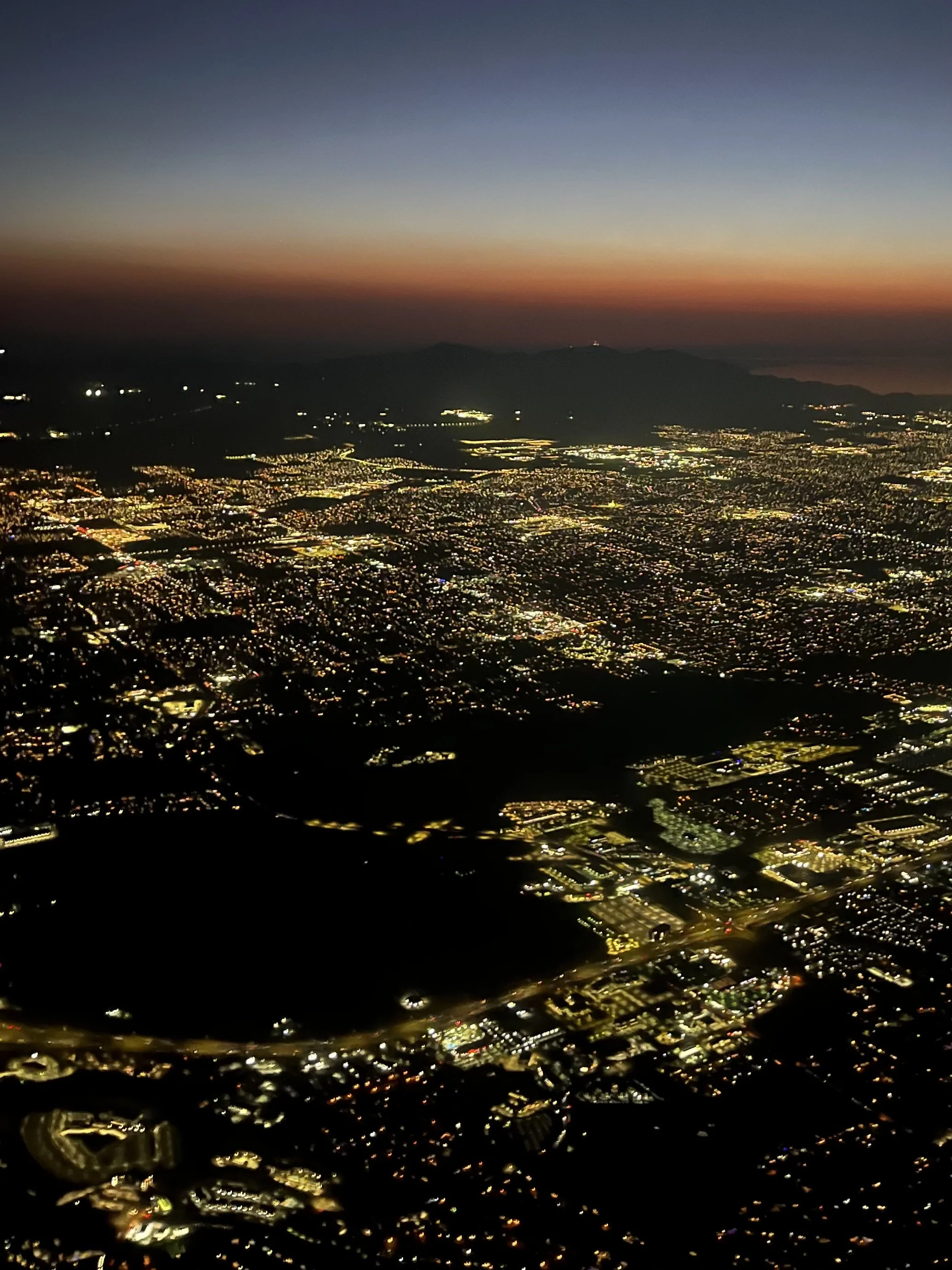 Aerial view of a city at dusk with a dark sky, city lights, and distant mountains.