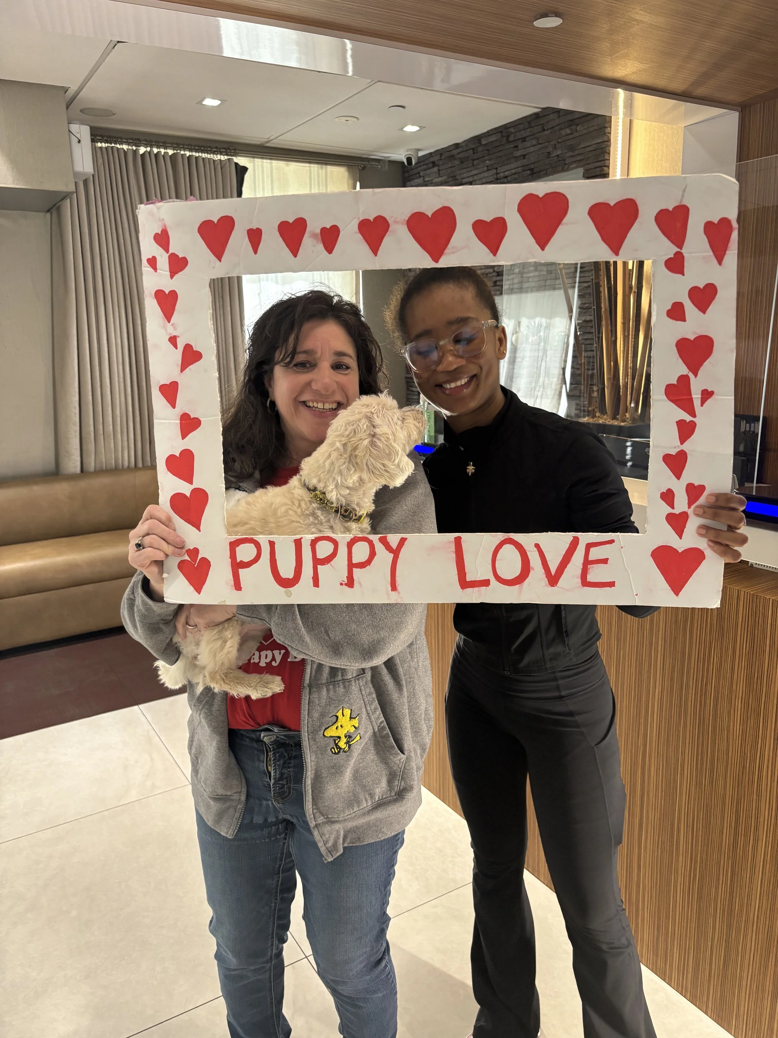 Two women smiling and holding a puppy inside a decorated frame with hearts and the words 'Puppy Love' on it.