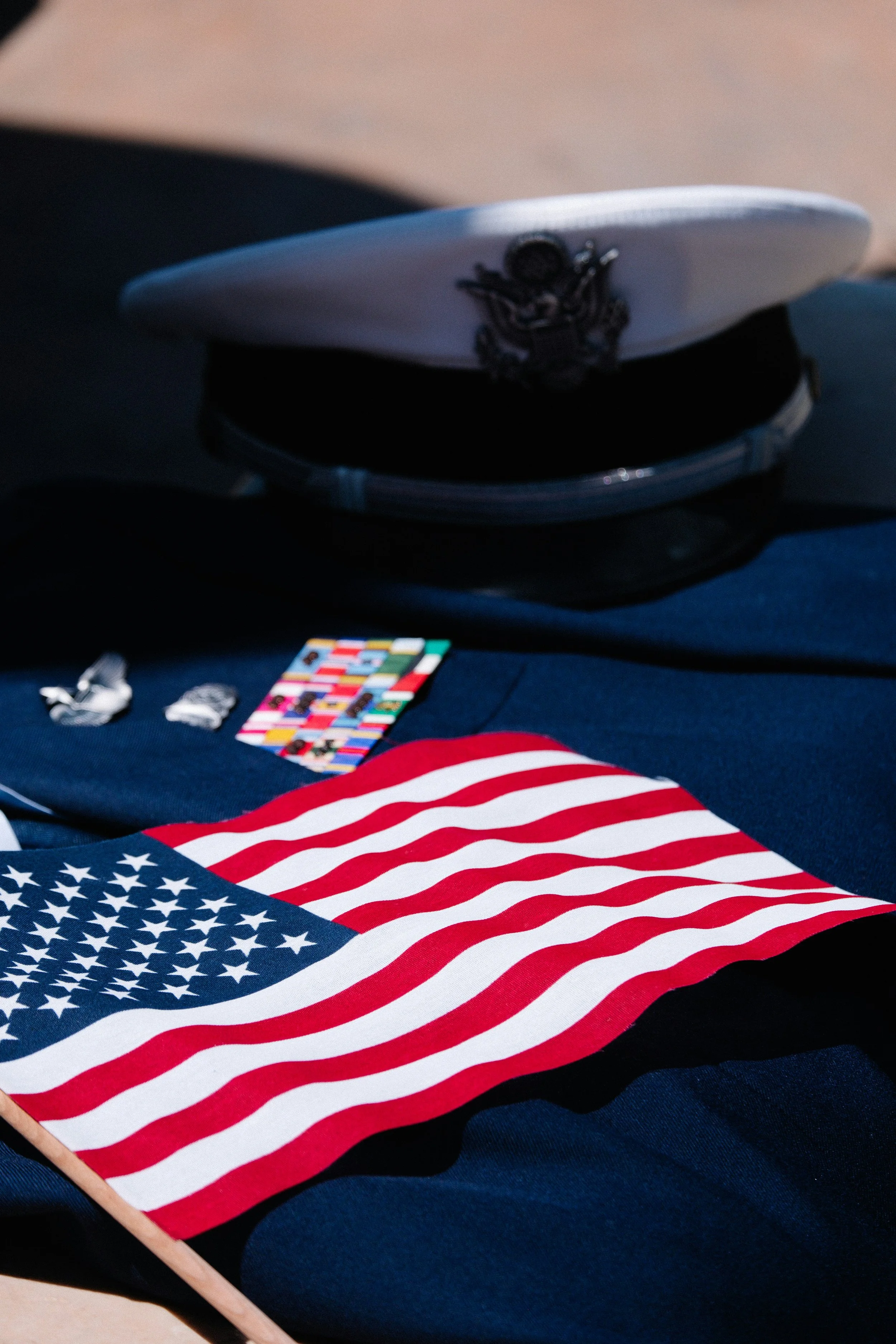 A United States military officer's hat, an American flag, and military insignia on a dark cloth surface, likely at a patriotic or memorial event.