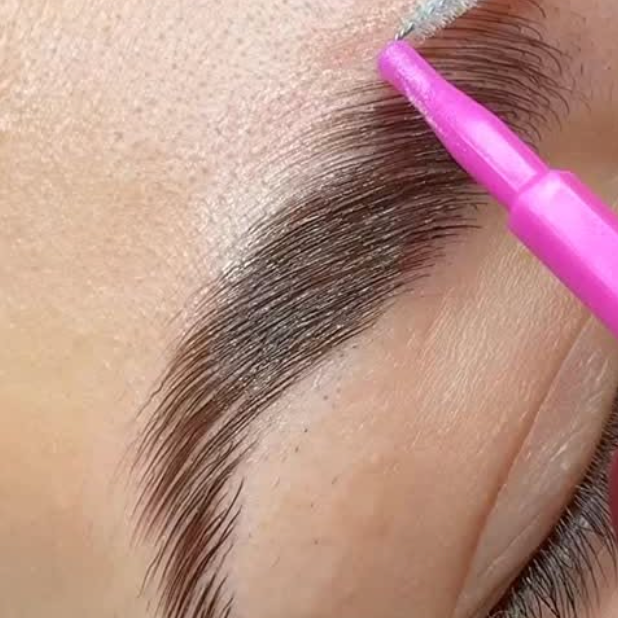 Close-up of a person’s eyebrow with a pink precision applicator applying eyebrow dye or ink.