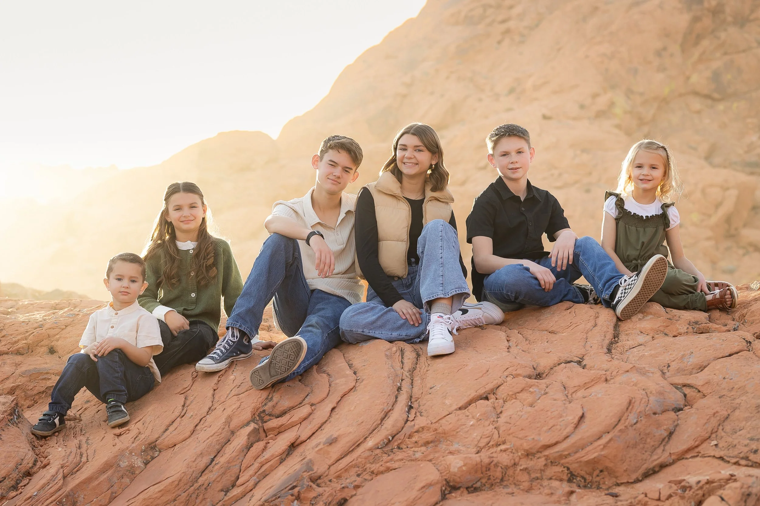 Seven children sitting on red rocks in a desert landscape during sunset.
