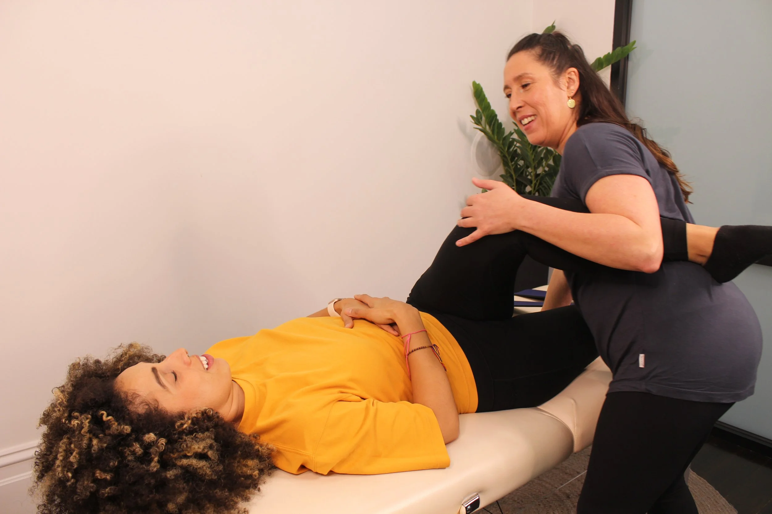 female stretch therapist stretching a woman in a yellow top on a massage table