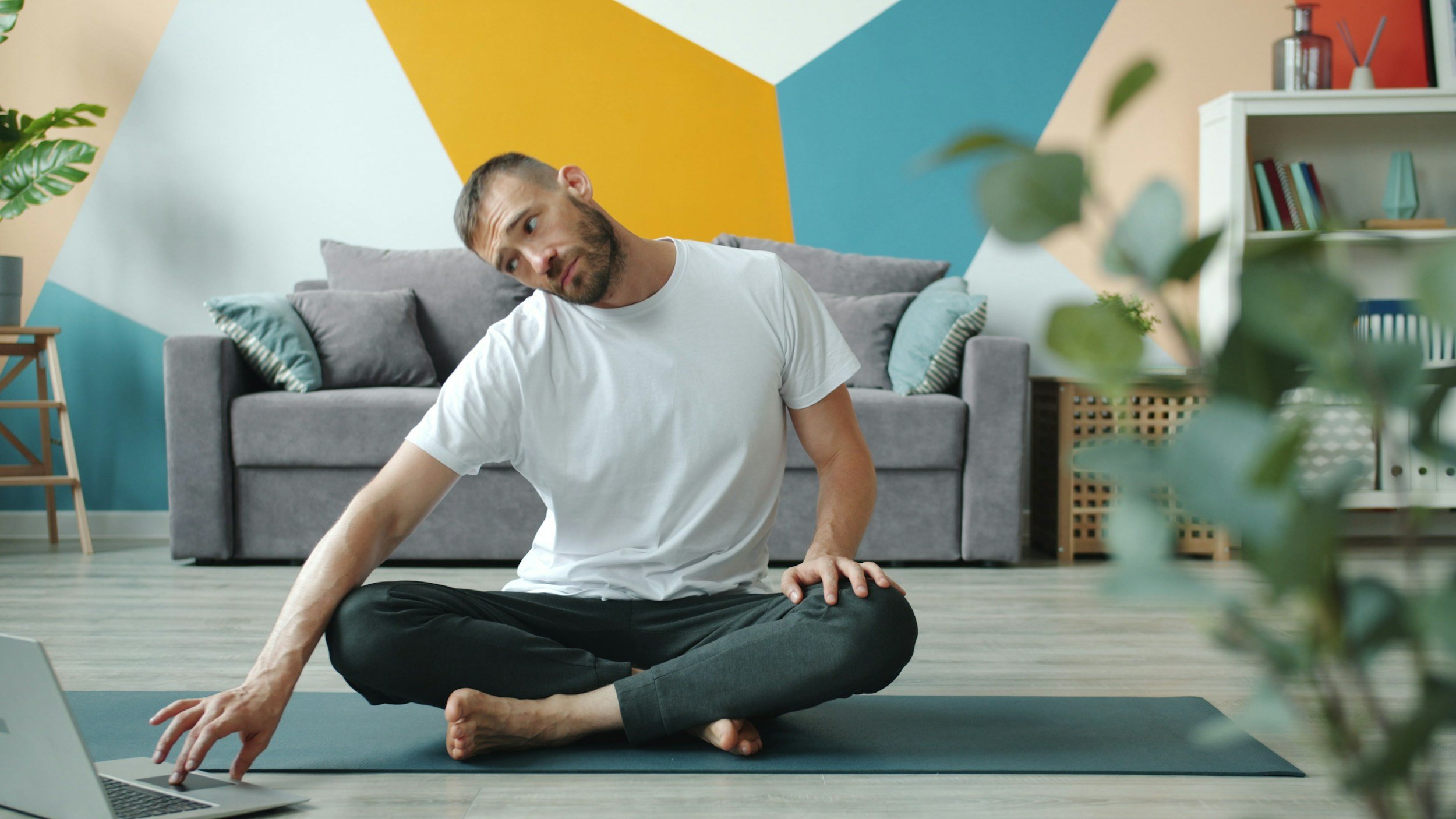 man stretching his neck while also on a computer sitting on a yoga mat