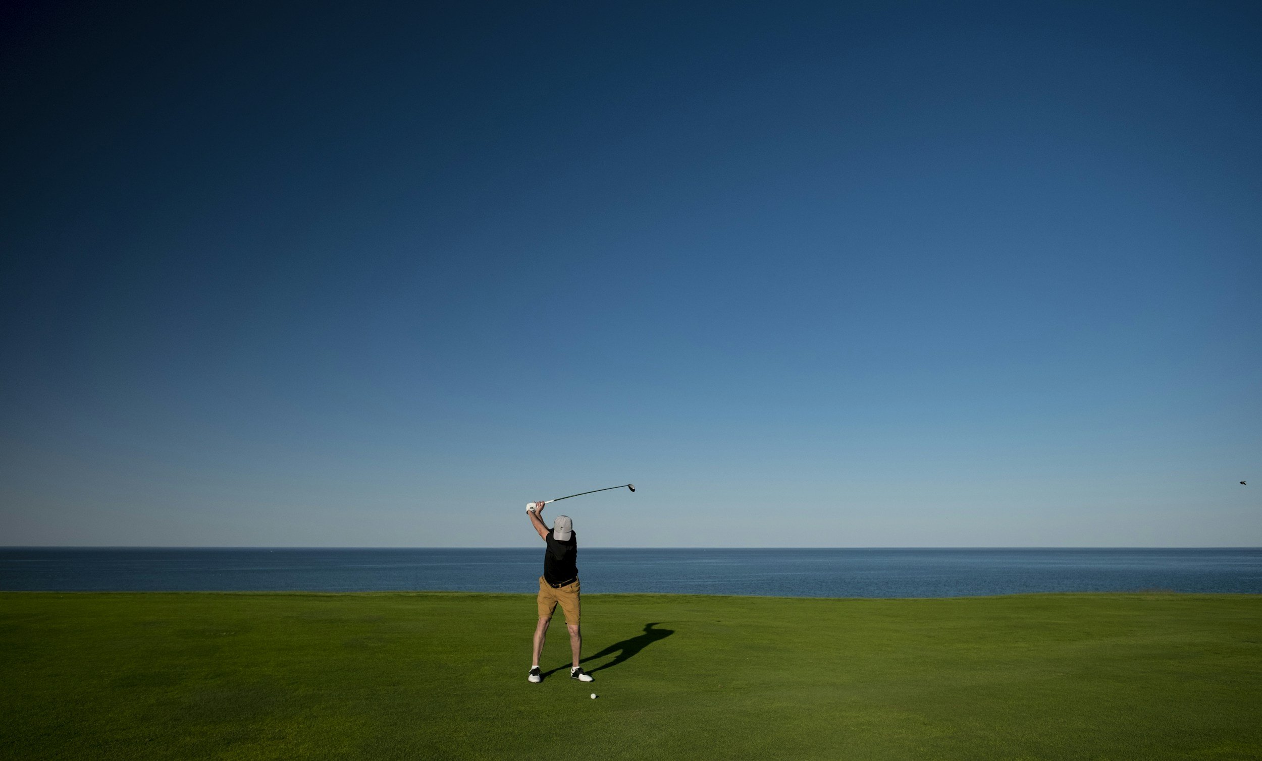 man swinging his golf club on a course right by the ocean