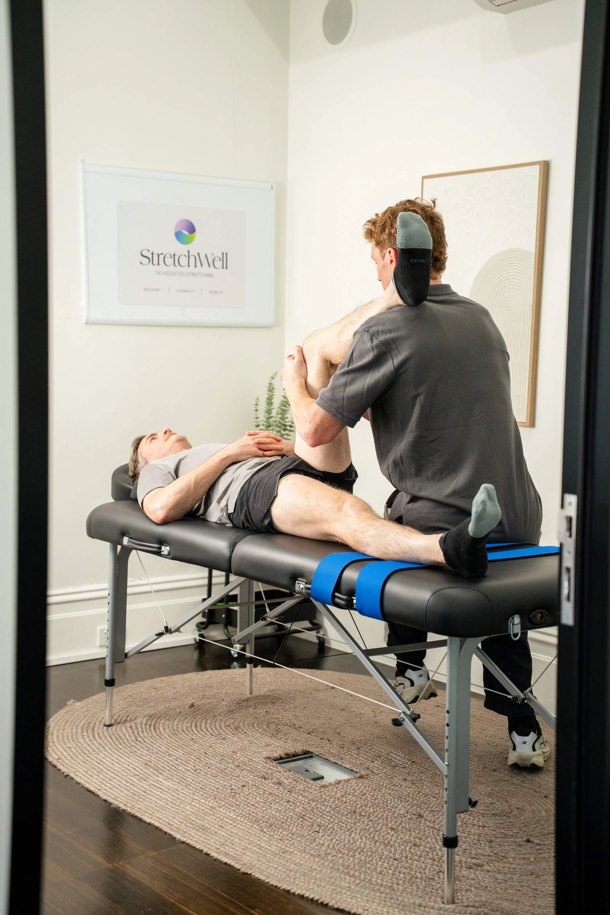 stretch therapist performing stretch therapy on a male client on a massage table