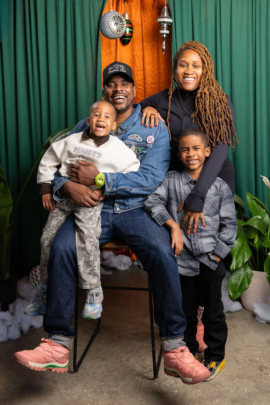 A happy family of five posing for a photo in front of a festive backdrop with green and orange curtains and holiday decorations.