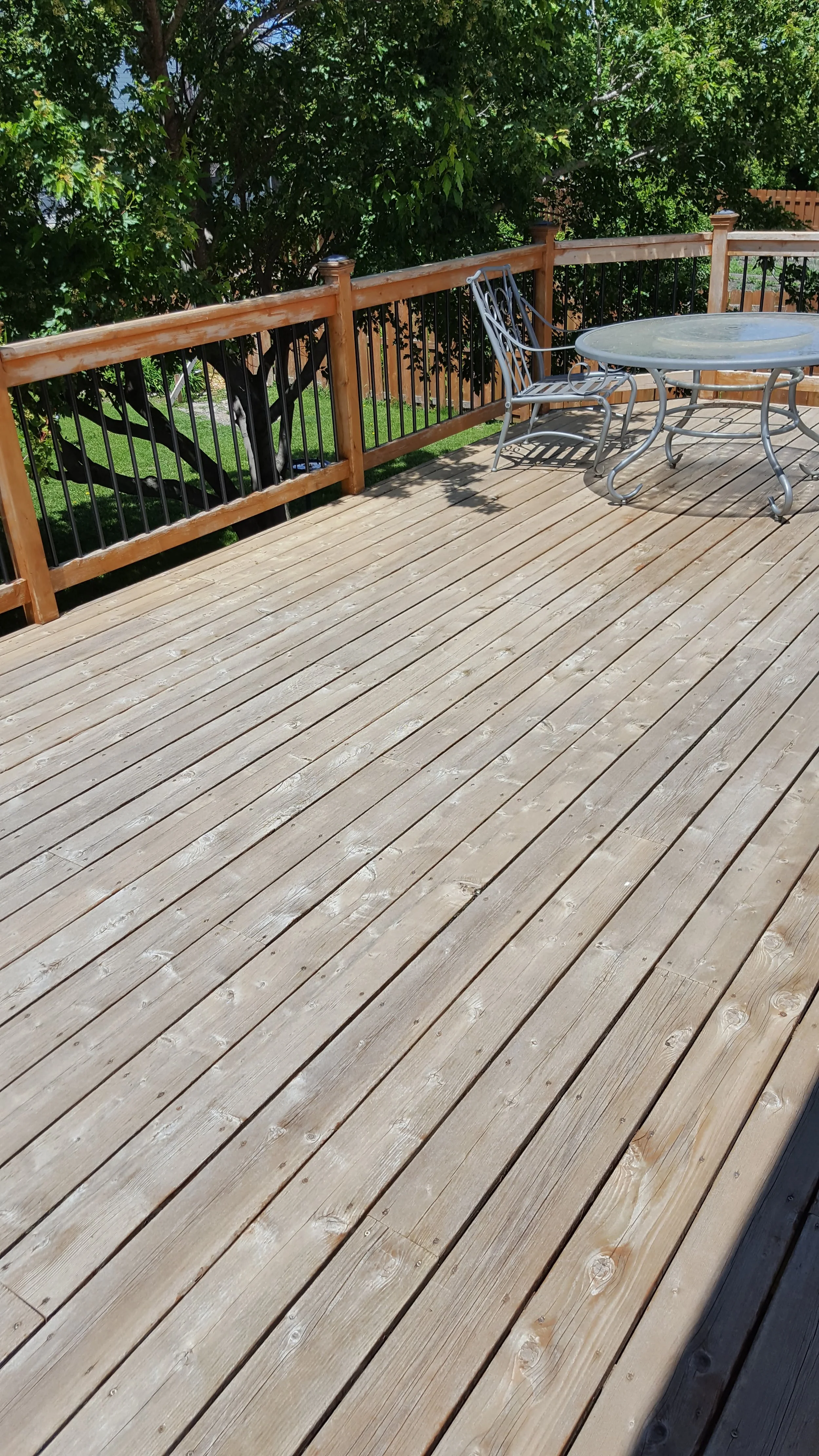 Wooden deck with a metal table and two metal chairs, surrounded by green trees and a wooden railing.