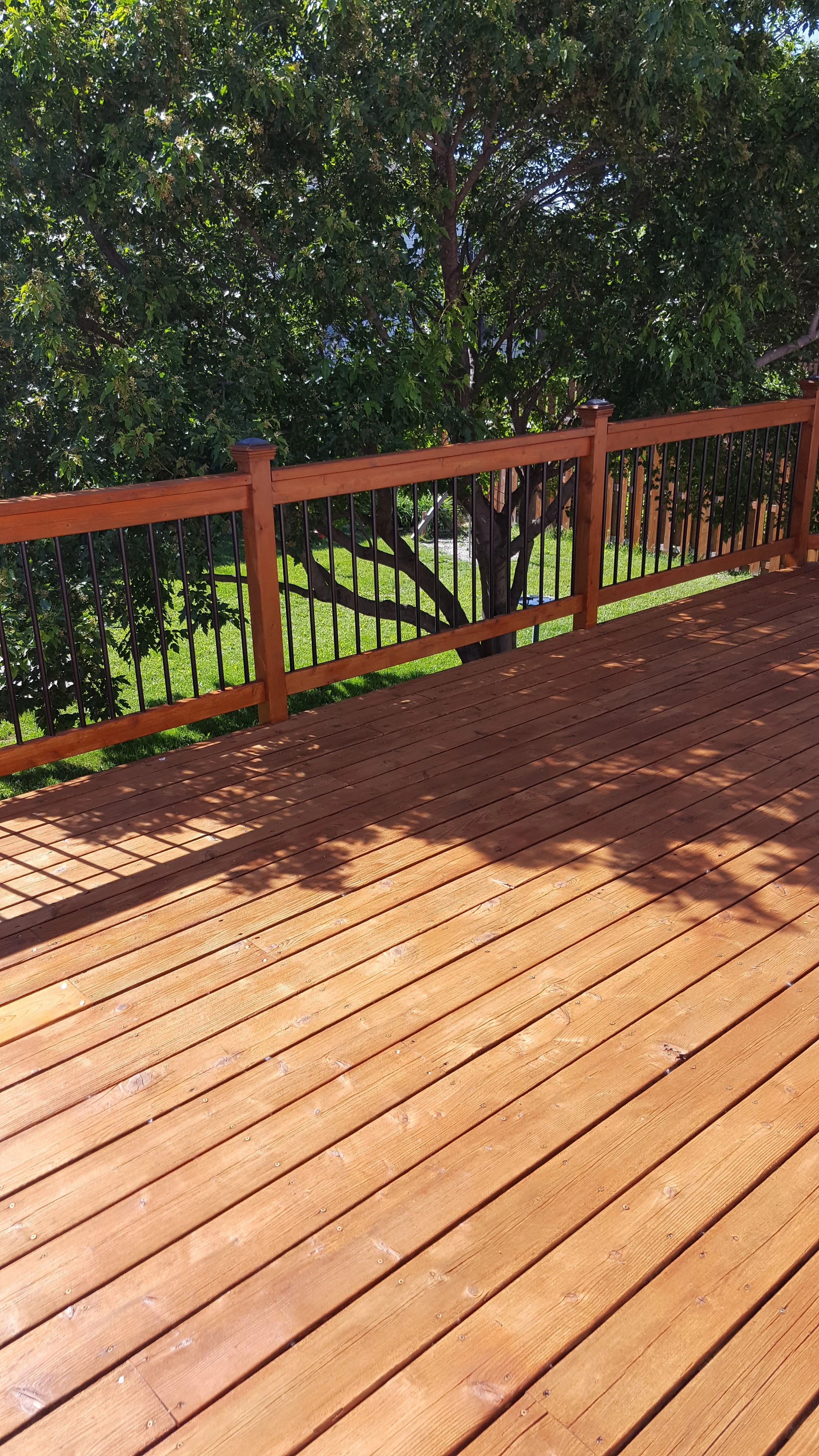 A wooden deck with a railing overlooking a yard with green grass and a large leafy tree.