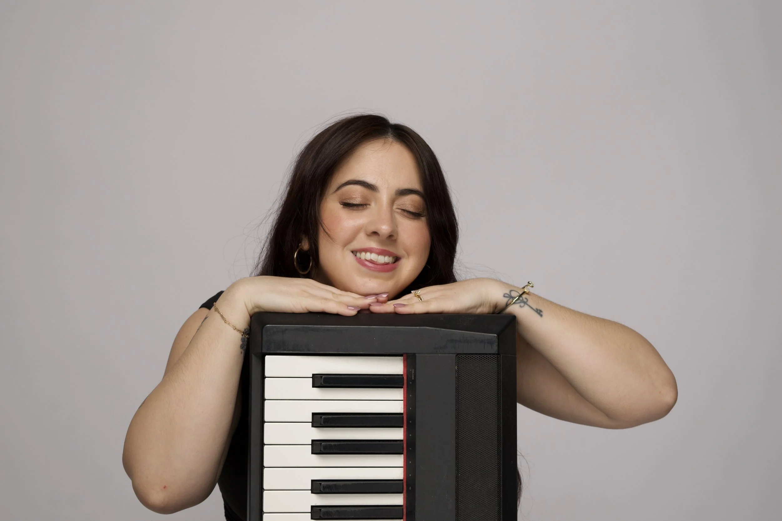 Founder Kate Elmendorf placeing here hands and head on a piano while smiling