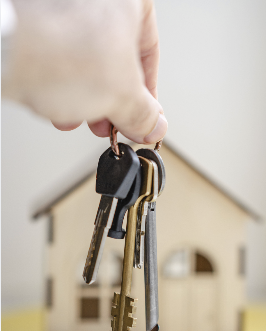 Close-up of a hand holding key rings with house keys in front of a small wooden house model.
